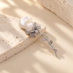 Silver-toned floral brooch with a baroque pearl bloom and sparkling leaf stem on stone