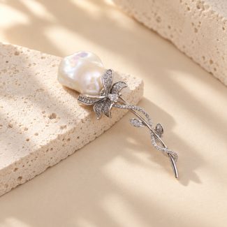 Silver-toned floral brooch with a baroque pearl bloom and sparkling leaf stem on stone
