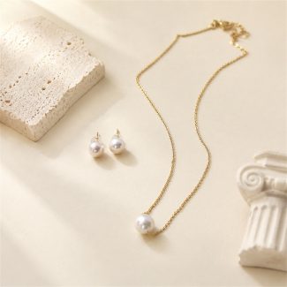 Single-pearl pendant necklace with matching pearl stud earrings laid flat