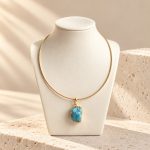 Turquoise oval pendant in a gold-tone frame on a smooth collar necklace, shown on a bust