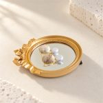 Brushed gold-tone disc and button pearl earrings reflected in a round mirror