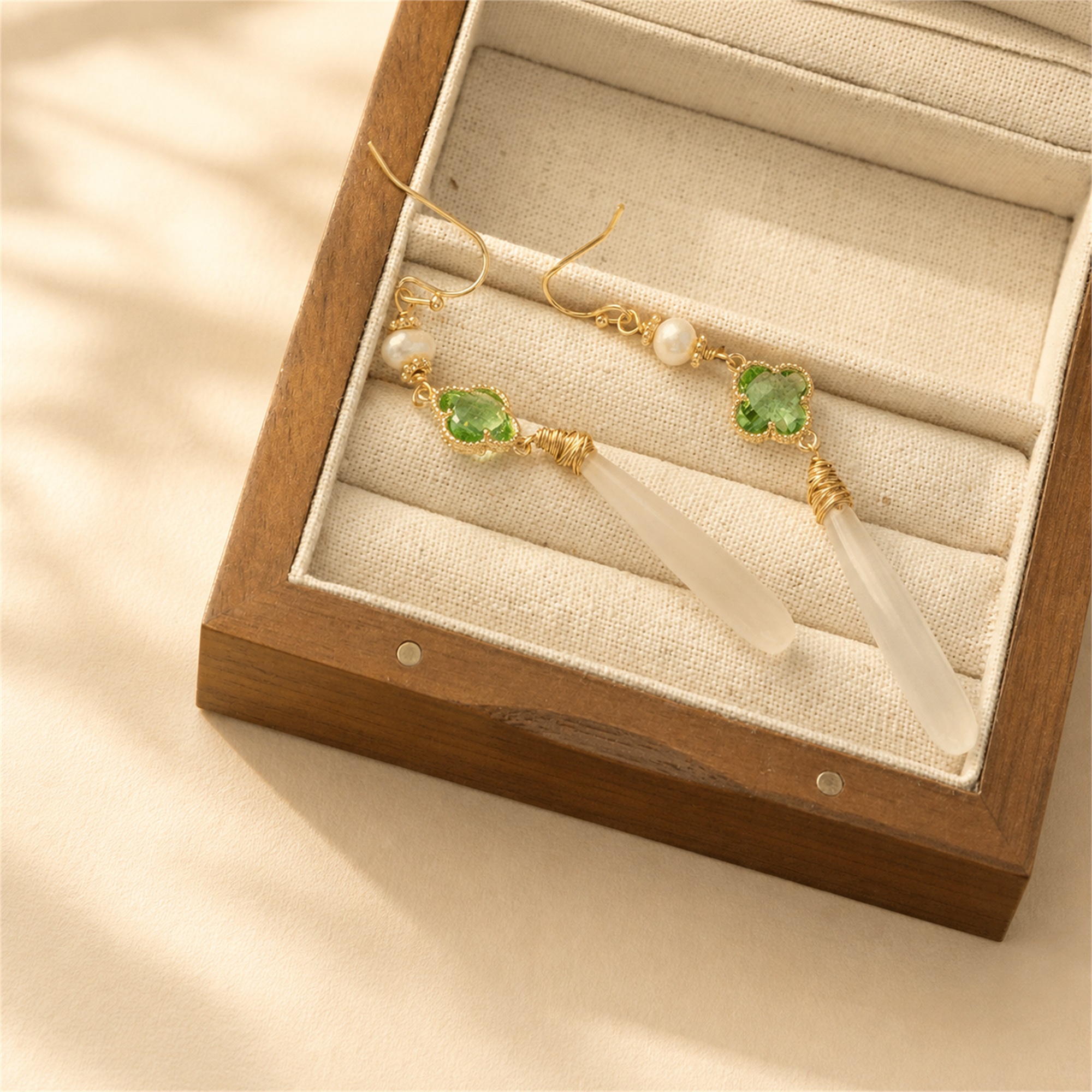 Green clover and white jade drop earrings resting in a display box