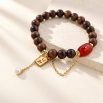 Close view of sandalwood beads, red agate and dangling pearl charm on an elastic bracelet