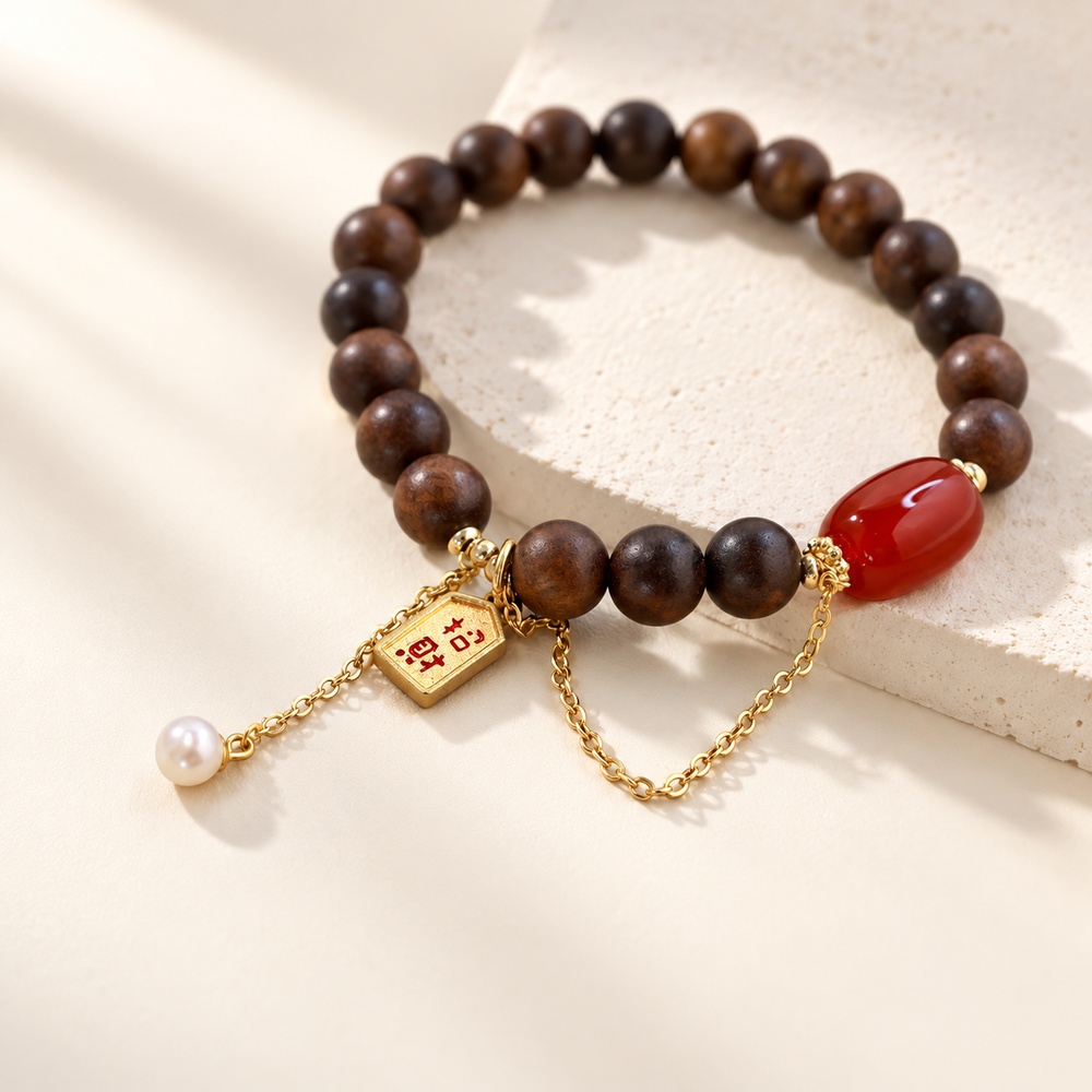 Close view of sandalwood beads, red agate and dangling pearl charm on an elastic bracelet