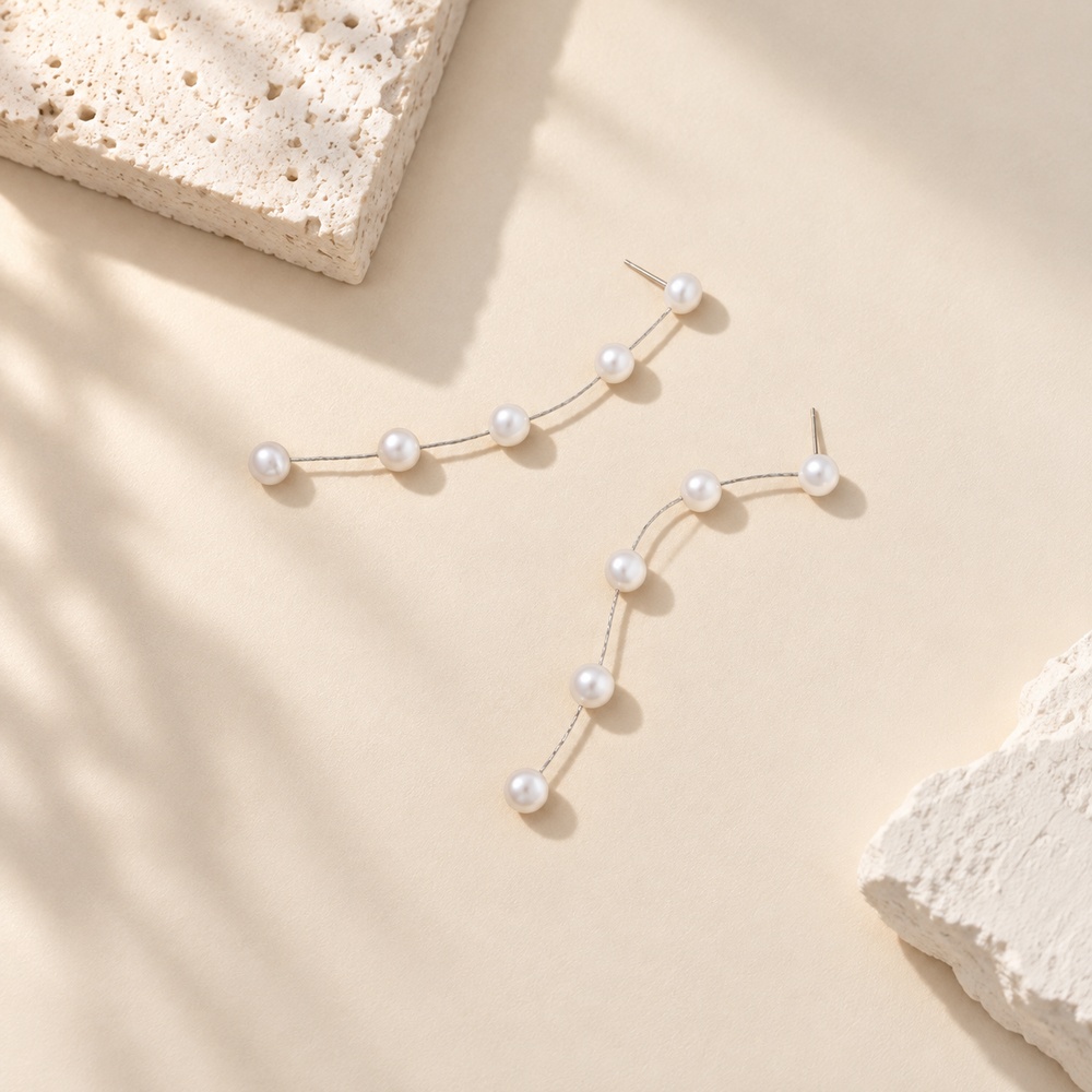 Pair of five-pearl linear drop earrings laid flat with fine metal chains