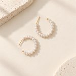 Freshwater pearl open hoop earrings laid flat, showing golden posts and curved pearl rows