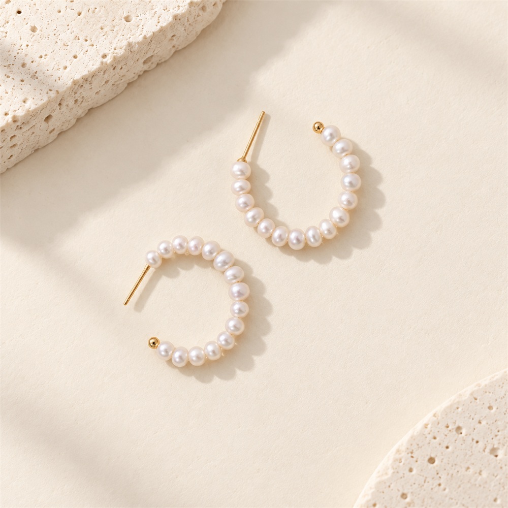 Freshwater pearl open hoop earrings laid flat, showing golden posts and curved pearl rows