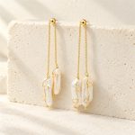 Baroque pearl drop earrings hanging from gold-toned chains, with curled wire details and staggered pearl lengths