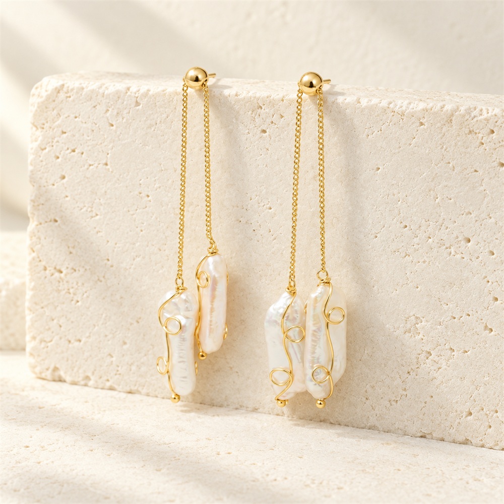 Baroque pearl drop earrings hanging from gold-toned chains, with curled wire details and staggered pearl lengths