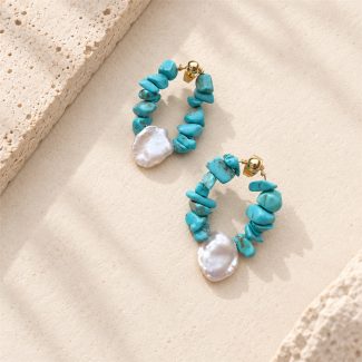 Turquoise chip teardrop hoop earrings with white pearl accents on a stone display