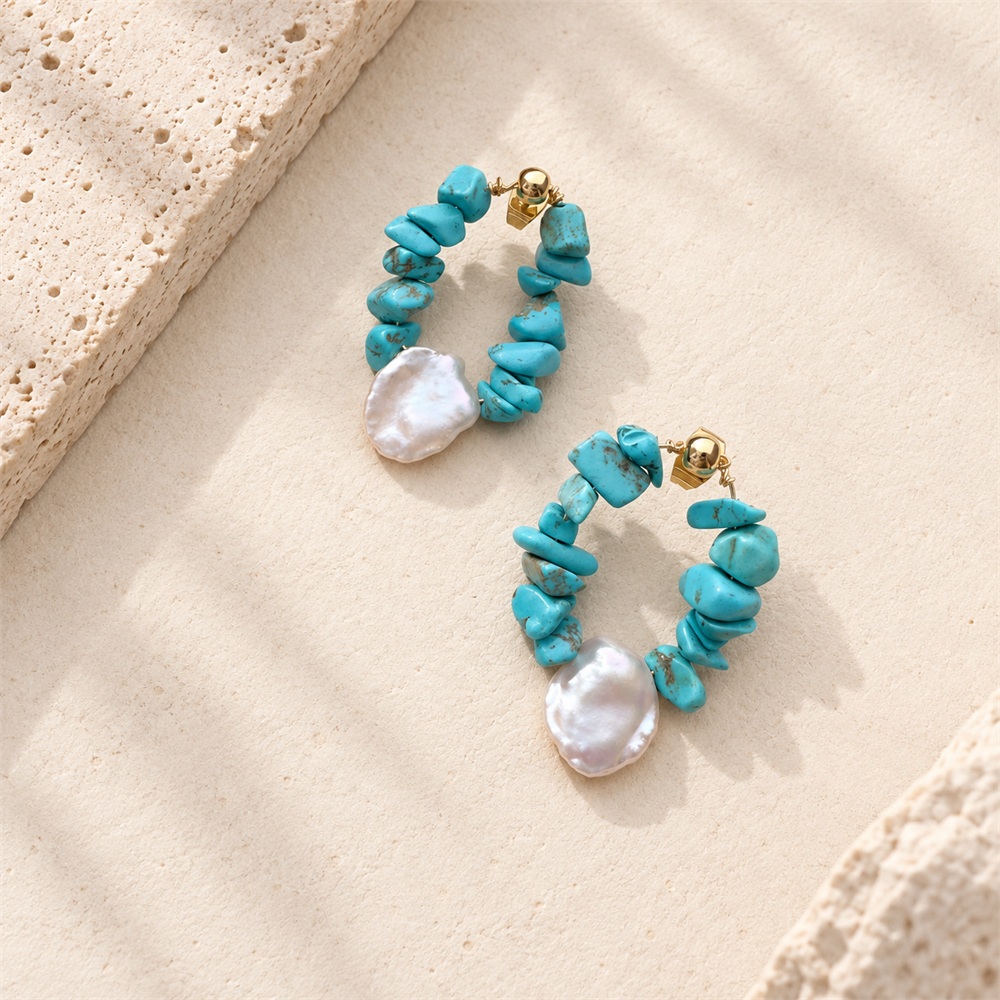Turquoise chip teardrop hoop earrings with white pearl accents on a stone display