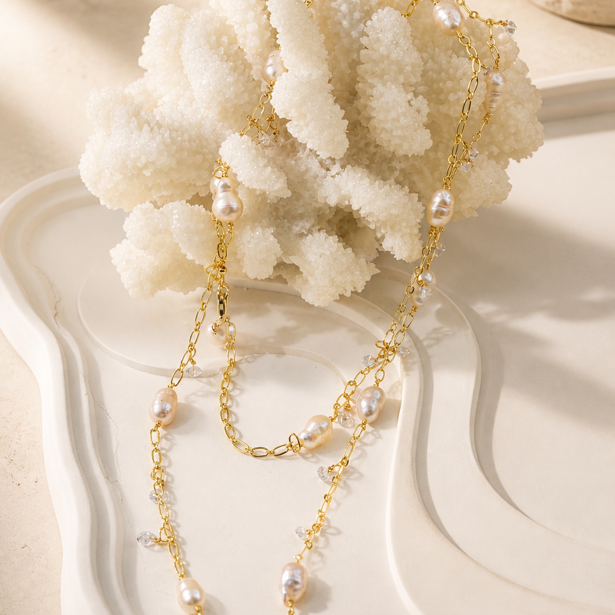 Close view of a gold-tone long necklace with irregular pearls and small clear dangling charms