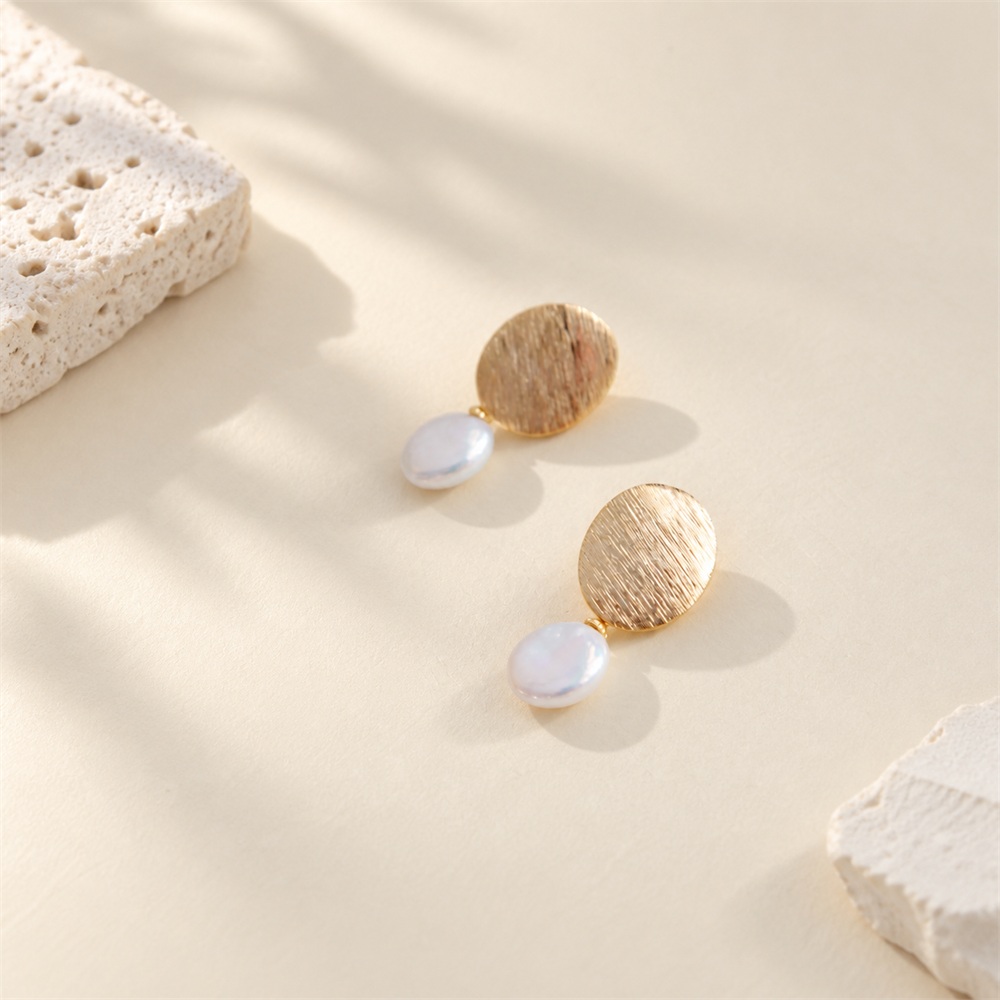Pair of brushed disc freshwater pearl drop earrings laid flat