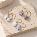 White rhombus and white and purple star-shaped pearl earrings arranged on a stone plate