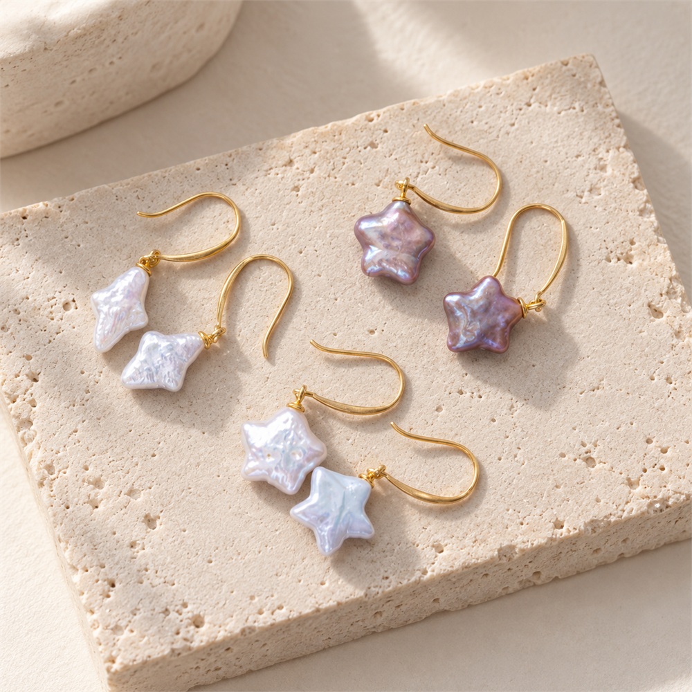 White rhombus and white and purple star-shaped pearl earrings arranged on a stone plate