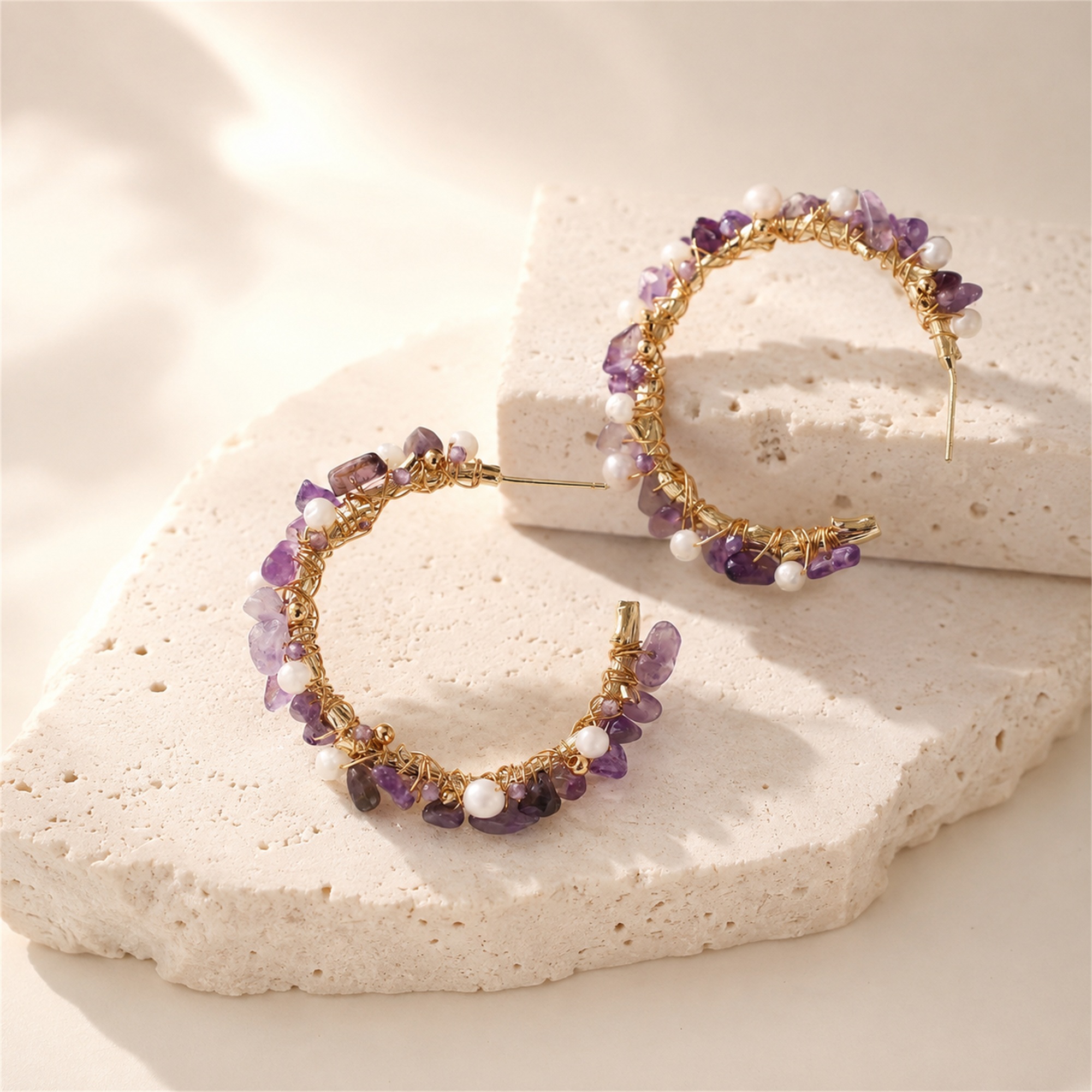 Amethyst and freshwater pearl hoop earrings displayed upright on a stone surface