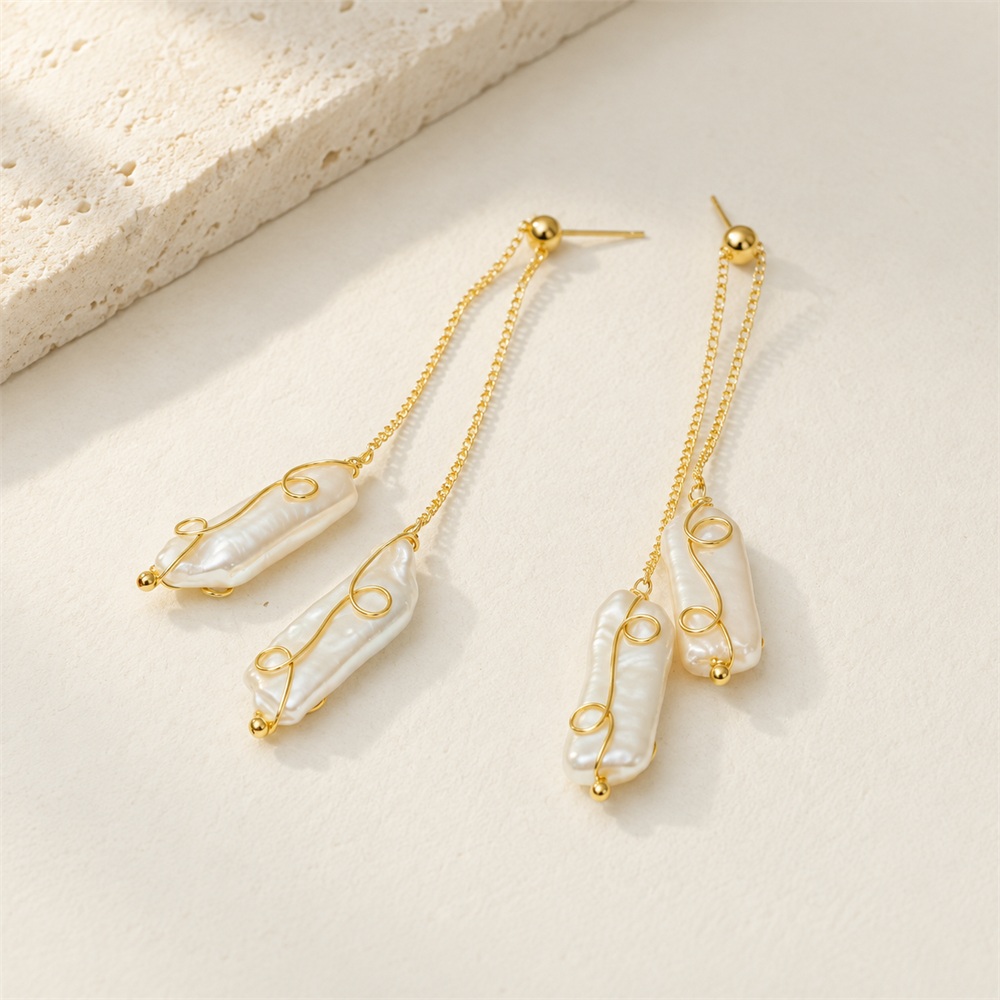Twin-drop pearl earrings laid flat, showing slender baroque pearls, gold-toned wire curls and stud posts