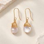 Close front view of wire-capped pearl hook earrings in a gold tone