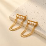 Gold-tone pearl bar and draped chain earrings beside a stone block