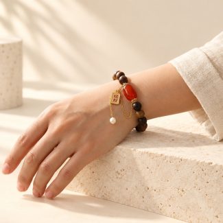 Sandalwood bead bracelet with red agate, inscribed charm and pearl drop worn on a wrist