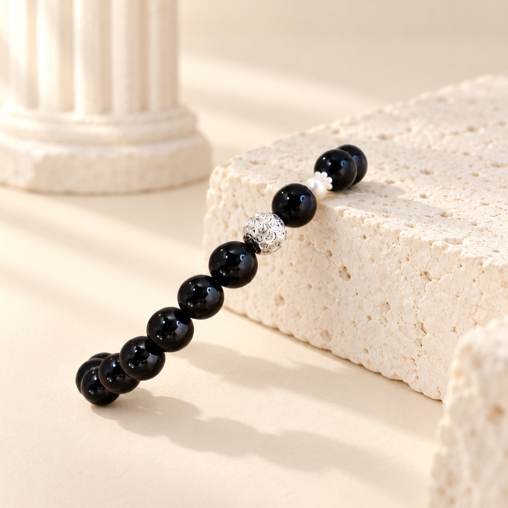Close view of black obsidian beads, small pearl and openwork silver-tone accent