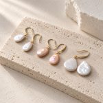 Three pairs of white and peach oval and teardrop pearl earrings with gold-toned hooks