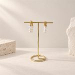 Freshwater pearl huggie hoop earrings shown from the side on a gold-toned display stand