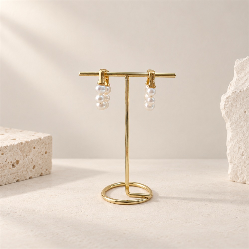 Freshwater pearl huggie hoop earrings shown from the side on a gold-toned display stand