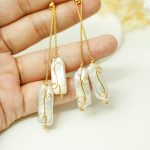 Baroque pearl chain earrings held against a hand, showing elongated pearls and adjustable staggered drops