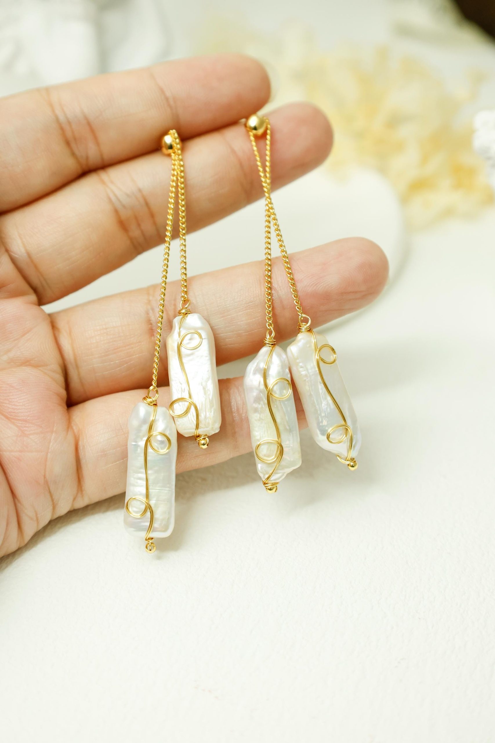Baroque pearl chain earrings held against a hand, showing elongated pearls and adjustable staggered drops