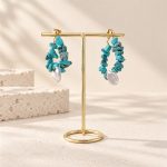 Turquoise chip pearl teardrop hoop earrings hanging from a gold display stand