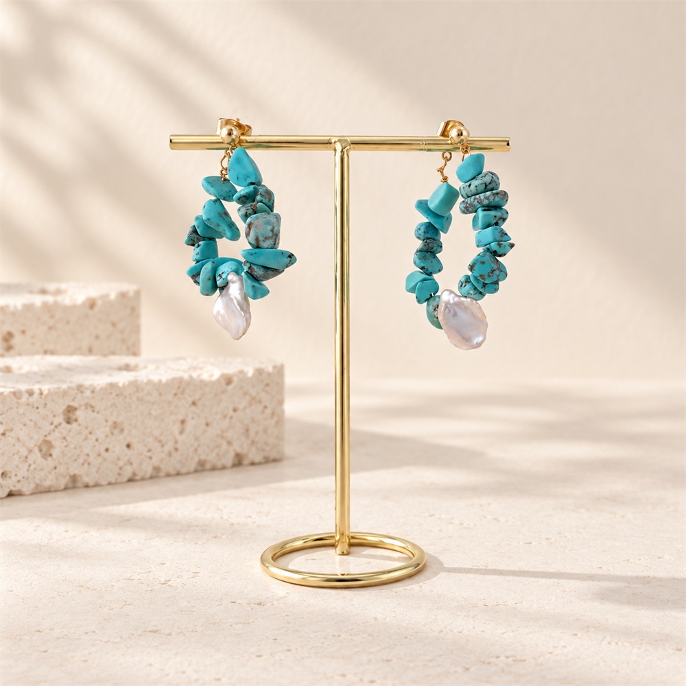 Turquoise chip pearl teardrop hoop earrings hanging from a gold display stand