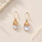 Angled view of pearl hook drop earrings with wrapped gold-tone caps