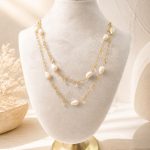 Long freshwater pearl necklace with spaced pearls and clear charms, layered on a display bust