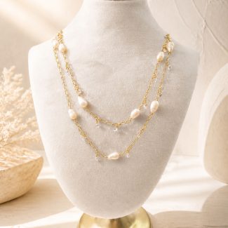 Long freshwater pearl necklace with spaced pearls and clear charms, layered on a display bust