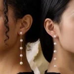 Two models wearing five-pearl long linear drop earrings in different metal tones