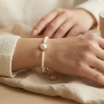 Model wearing a fine pearl bracelet with one larger pearl in a gold-tone bezel