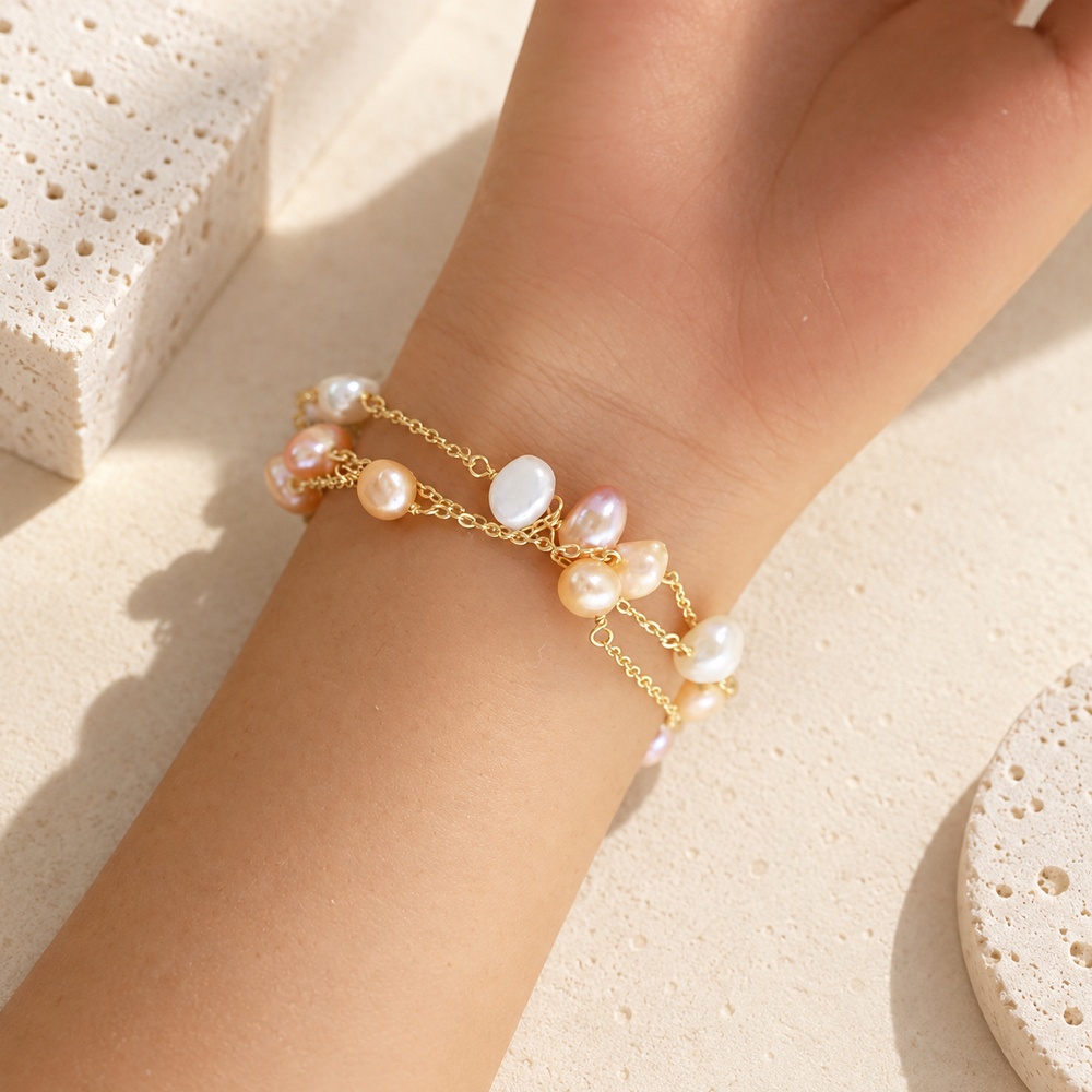 Close wrist view of a triple-chain bracelet with scattered peach and white pearls