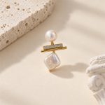 Close-up of one earring with a round pearl, sparkling horizontal bar and square pearl drop