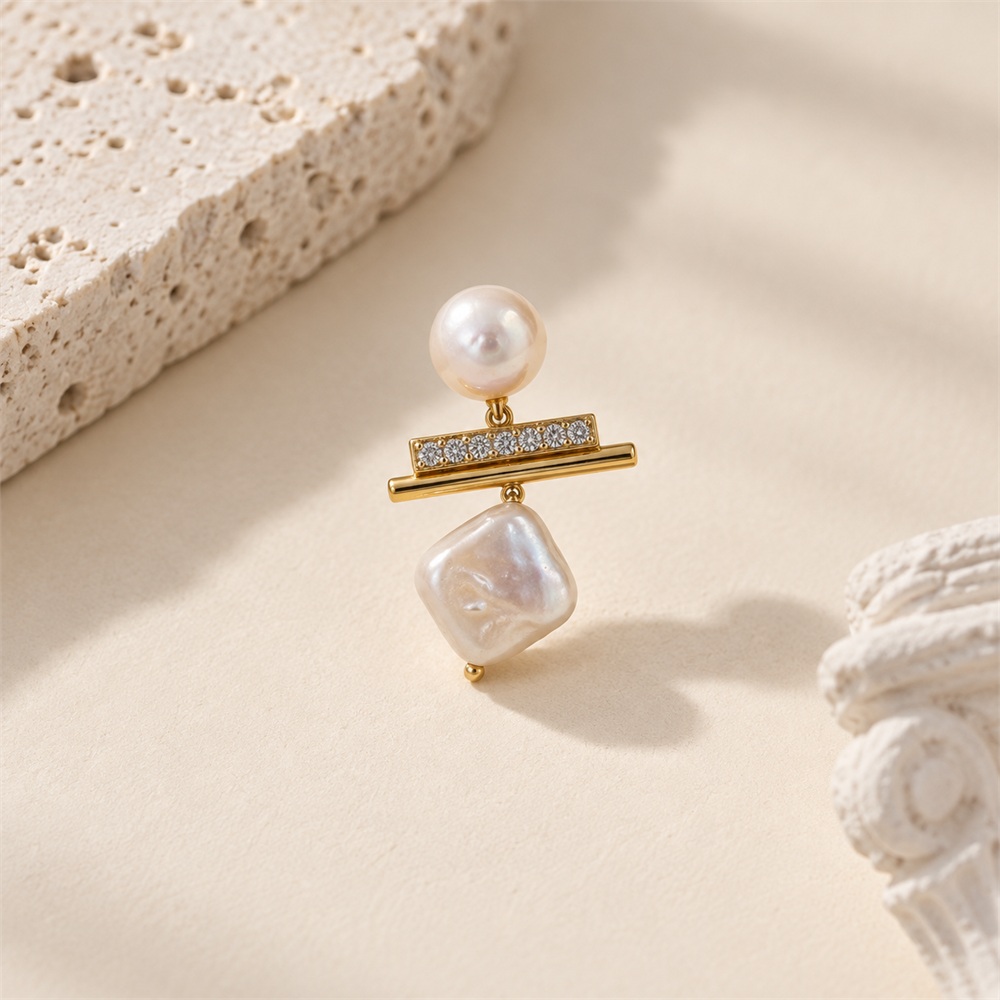 Close-up of one earring with a round pearl, sparkling horizontal bar and square pearl drop