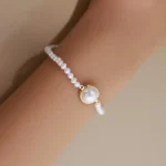 Close wrist view of the bezel-set centre pearl on a fine beaded bracelet