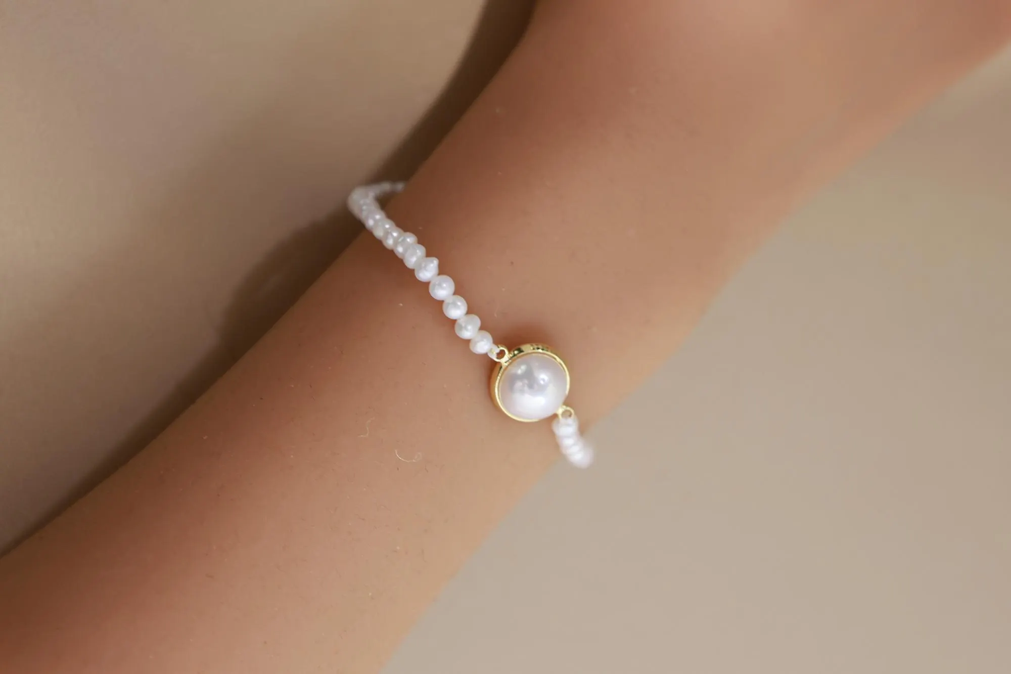 Close wrist view of the bezel-set centre pearl on a fine beaded bracelet