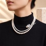 Baroque pearl floral brooch pinned beside a layered pearl necklace on a black top