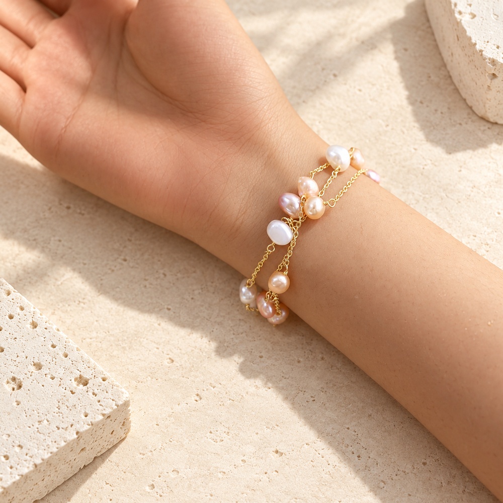 Triple-chain blush and white baroque pearl bracelet worn on a wrist