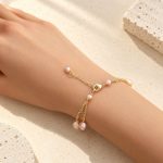 Lobster clasp and pearl-tipped extender of a blush pearl triple-chain bracelet on a wrist