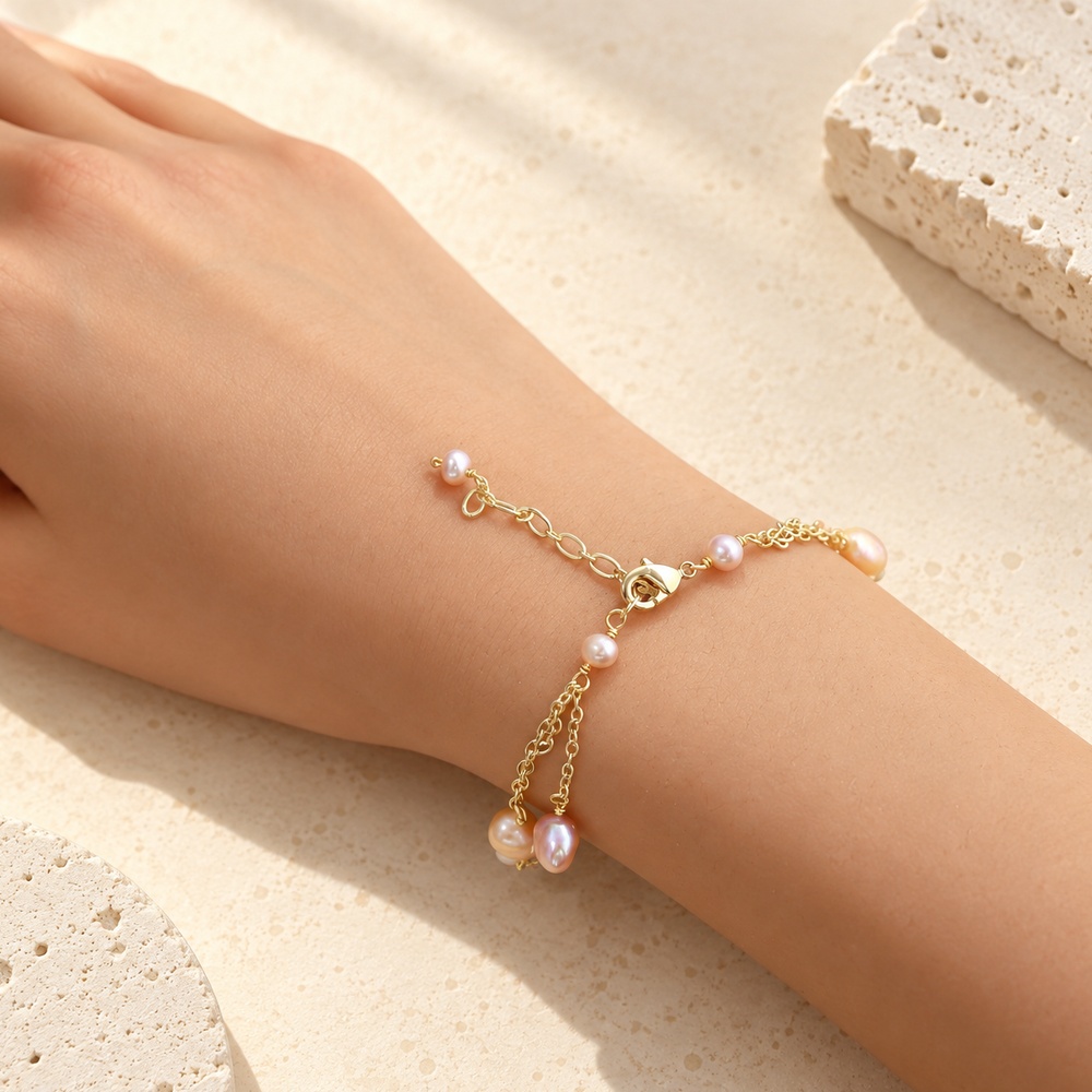 Lobster clasp and pearl-tipped extender of a blush pearl triple-chain bracelet on a wrist
