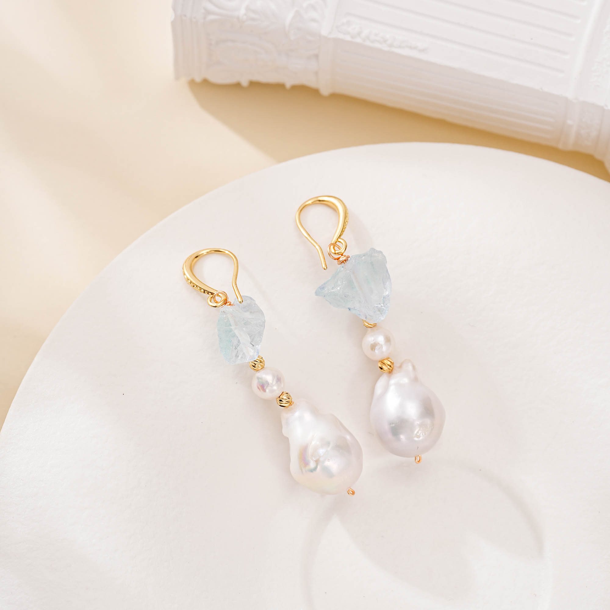 Aquamarine and baroque pearl drop earrings with gold-toned hooks on a white plate