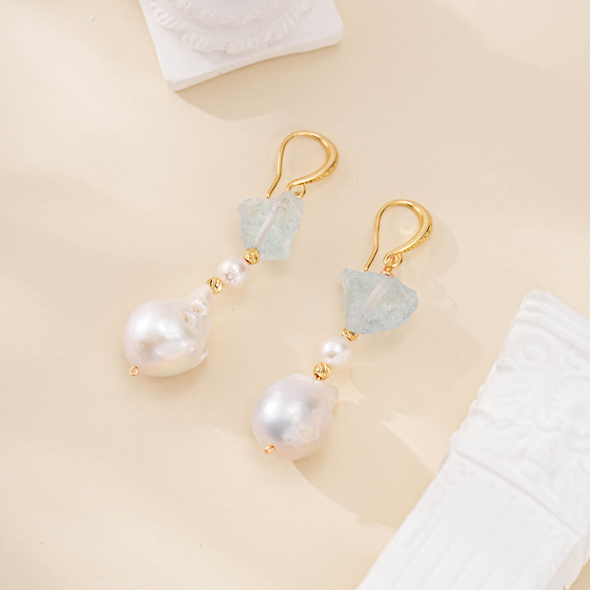 Pair of raw aquamarine and baroque pearl drop earrings laid flat