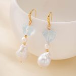 Close-up of aquamarine and baroque pearl drop earrings hanging on a white display