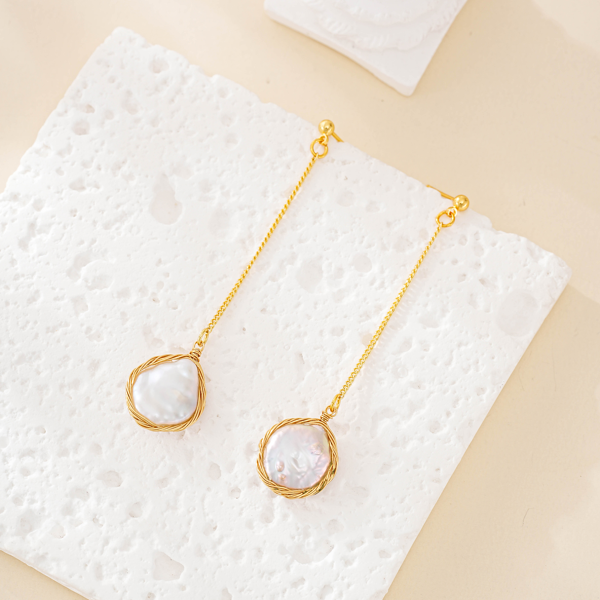 Pair of long baroque pearl chain drop earrings laid flat with wrapped pearl frames